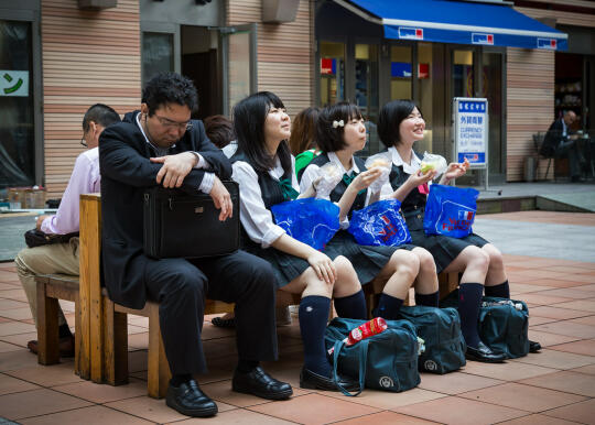 Schoolchildren and a businessman sharing a bench