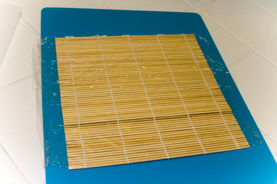 A bamboo sushi mat on a blue cutting board