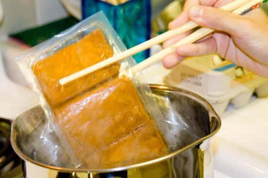 Putting the package of aburaáge in the pot of boiling water